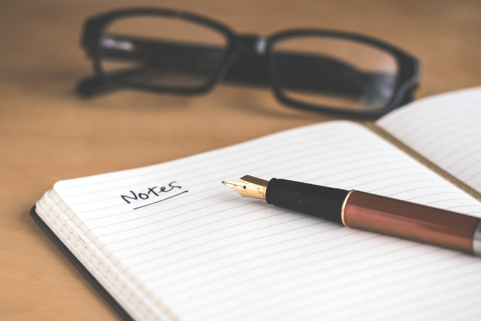 Fountain pen resting on an open notebook beside reading glasses on a desk
